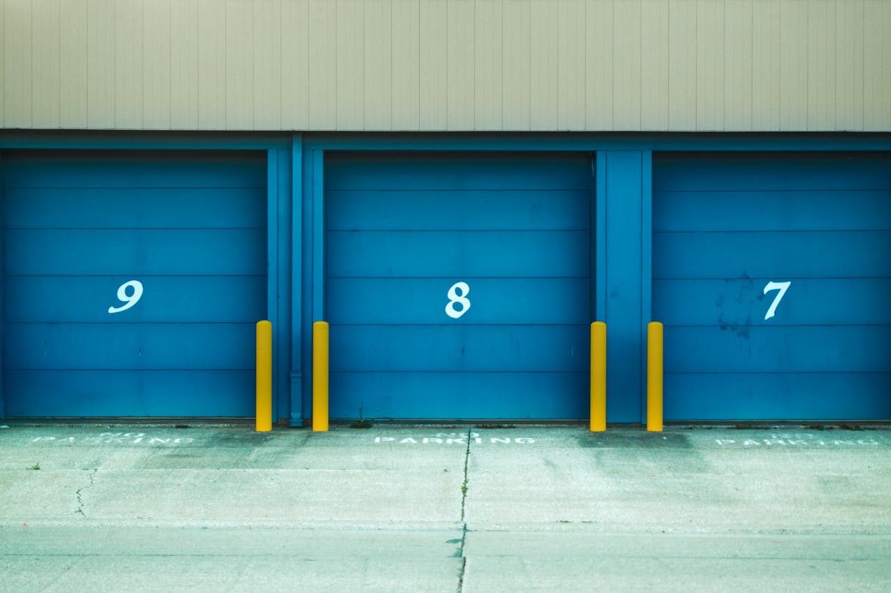 Three blue shutter doors numbered 9, 8, and 7 with yellow barriers in urban environment.